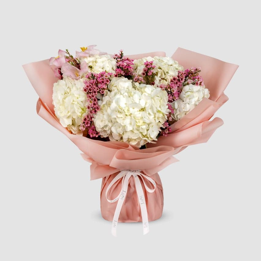  Gentle Hug – White hydrangeas, purple wax flowers, and pink tulips bouquet.