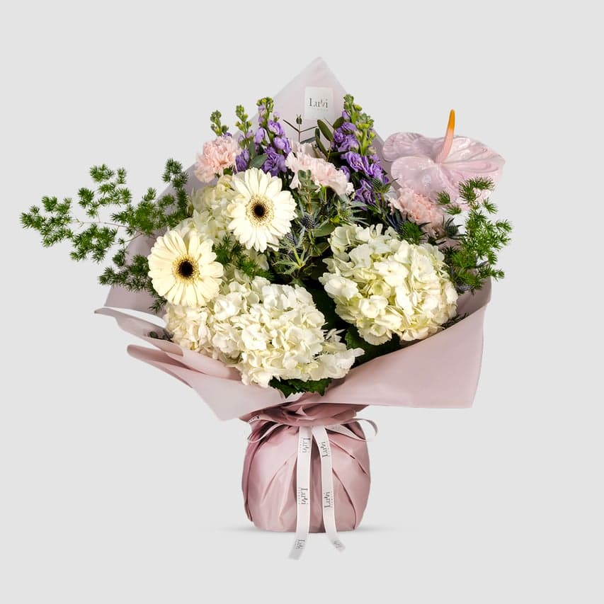 Appreciation Petals bouquet featuring white gerberas, purple sprayed anthuriums, purple matthiola, blue eryngium, pink carnations, asparagus, and white hydrangeas	
